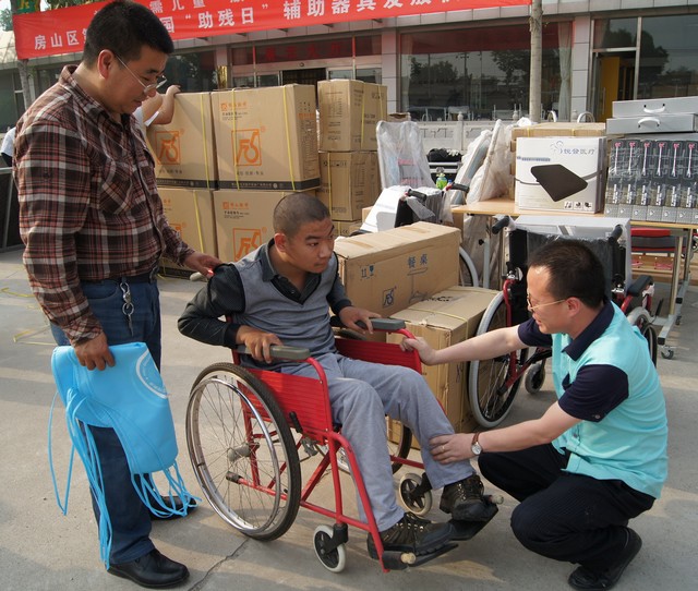 技术人员为家长和残疾少年演示如何正确使用轮椅