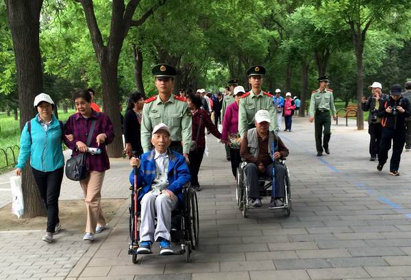 图为武警战士推着老年残疾人逛公园