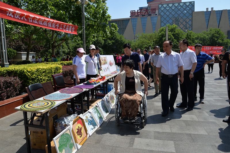 图为市残联副理事长欧玲参观残疾人书法绘画手工艺品